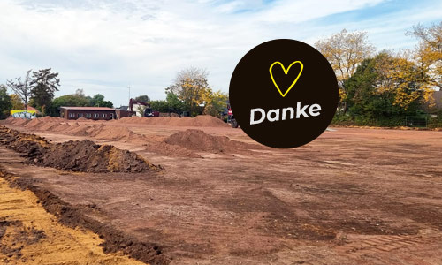 Erdarbeiten am Sportplatz<br />
Baufortschritt am neuen Sportplatz des SV Merbeck: Erdarbeiten und aufgeschüttete Erdhügel auf dem weitläufigen Sportplatzgelände. Im Hintergrund sind Vereinsgebäude und Bäume zu sehen. Die Einblendung trägt den Schriftzug „Merbecker dürfen das“ mit gelbem Herz.