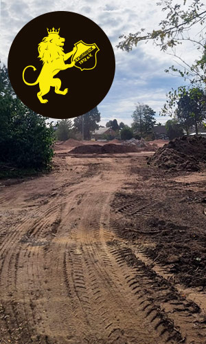 Baufortschritt / Zufahrt<br />
Bauarbeiten am neuen Sportplatz des SV Merbeck: Die freigelegte und mit schweren Fahrzeugen befahrene Zufahrt führt durch das zukünftige Sportplatzgelände. Oben links ist das Vereinswappen des SV Merbeck eingeblendet.